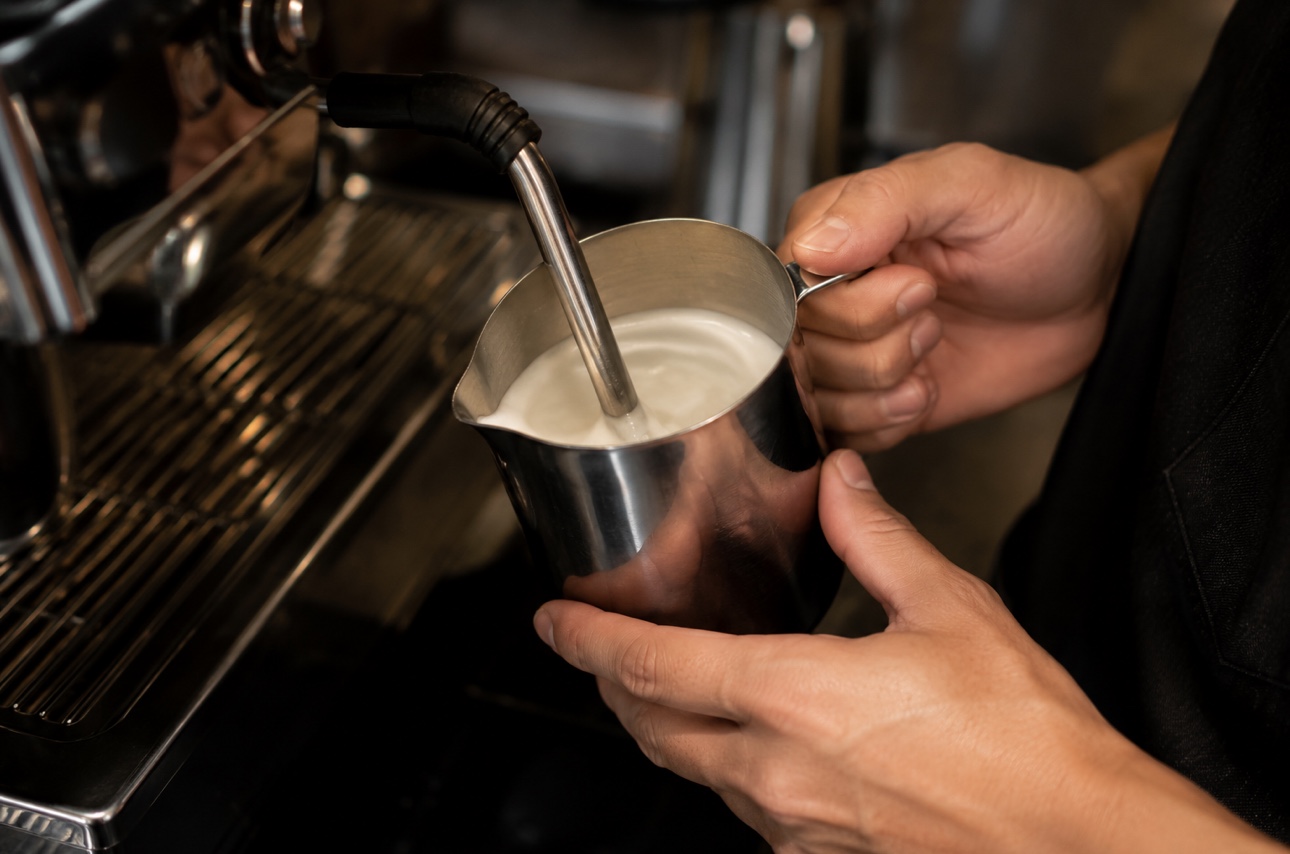A barista steaming milk in a pitcher to create smooth, creamy microfoam for a cappuccino.